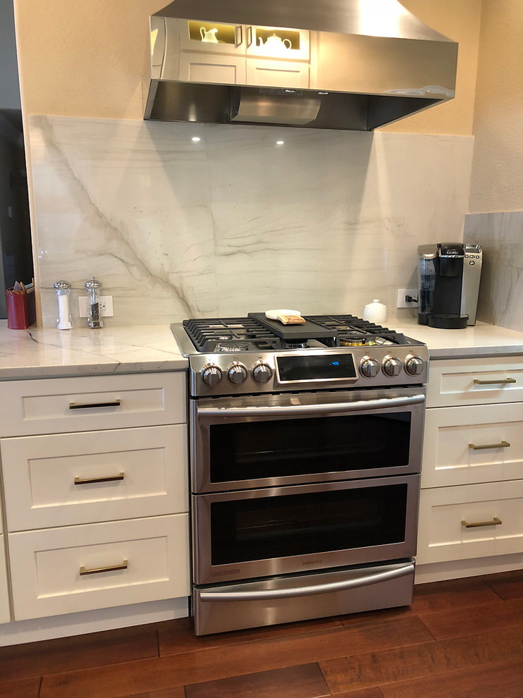 Inspiration for a large contemporary l-shaped kitchen in Austin with an undermount sink, shaker cabinets, white cabinets, quartzite benchtops, white splashback, stone slab splashback, stainless steel appliances, dark hardwood floors, with island, brown floor and white benchtop.
