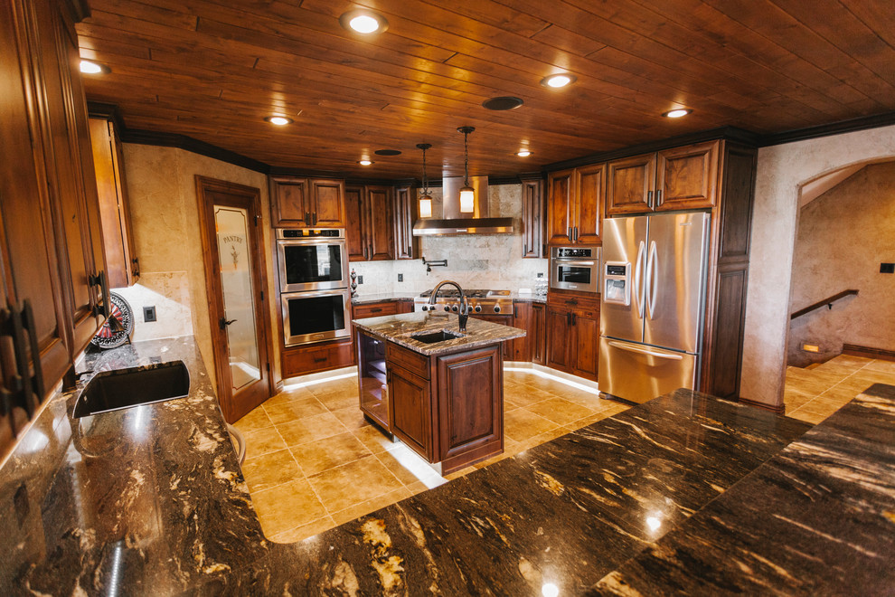 Large transitional u-shaped slate floor eat-in kitchen photo with a drop-in sink, recessed-panel cabinets, dark wood cabinets, granite countertops, beige backsplash, stone tile backsplash, stainless steel appliances, beige walls and an island