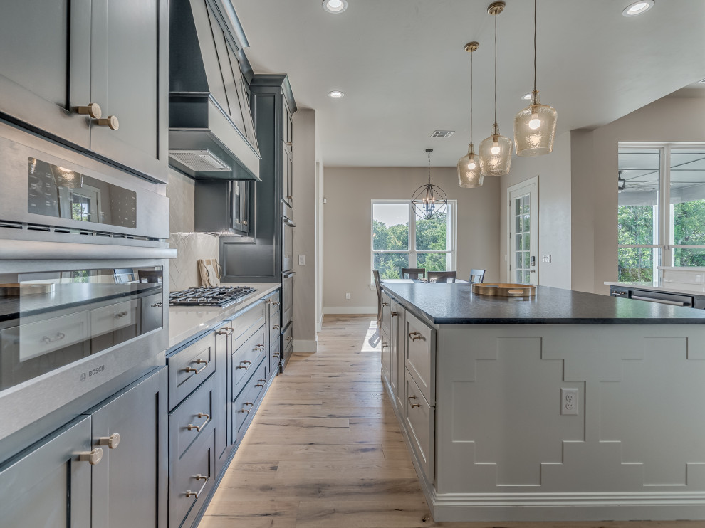 Photo of a large country kitchen in Oklahoma City with a drop-in sink, beaded inset cabinets, grey cabinets, white splashback, medium hardwood floors, with island and grey benchtop.