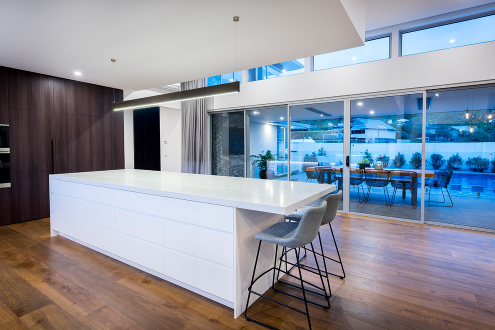 Expansive contemporary l-shaped open plan kitchen in Melbourne with an undermount sink, quartz benchtops, black appliances, medium hardwood floors, a peninsula, brown floor, white benchtop, flat-panel cabinets, dark wood cabinets and window splashback.