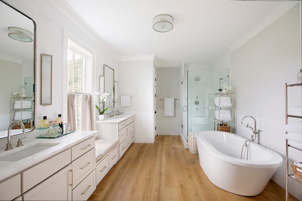 Design ideas for a transitional master bathroom in Charleston with a freestanding tub, a corner shower, an undermount sink, a hinged shower door, white benchtops, recessed-panel cabinets, white cabinets, white tile, grey walls, medium hardwood floors and brown floor.