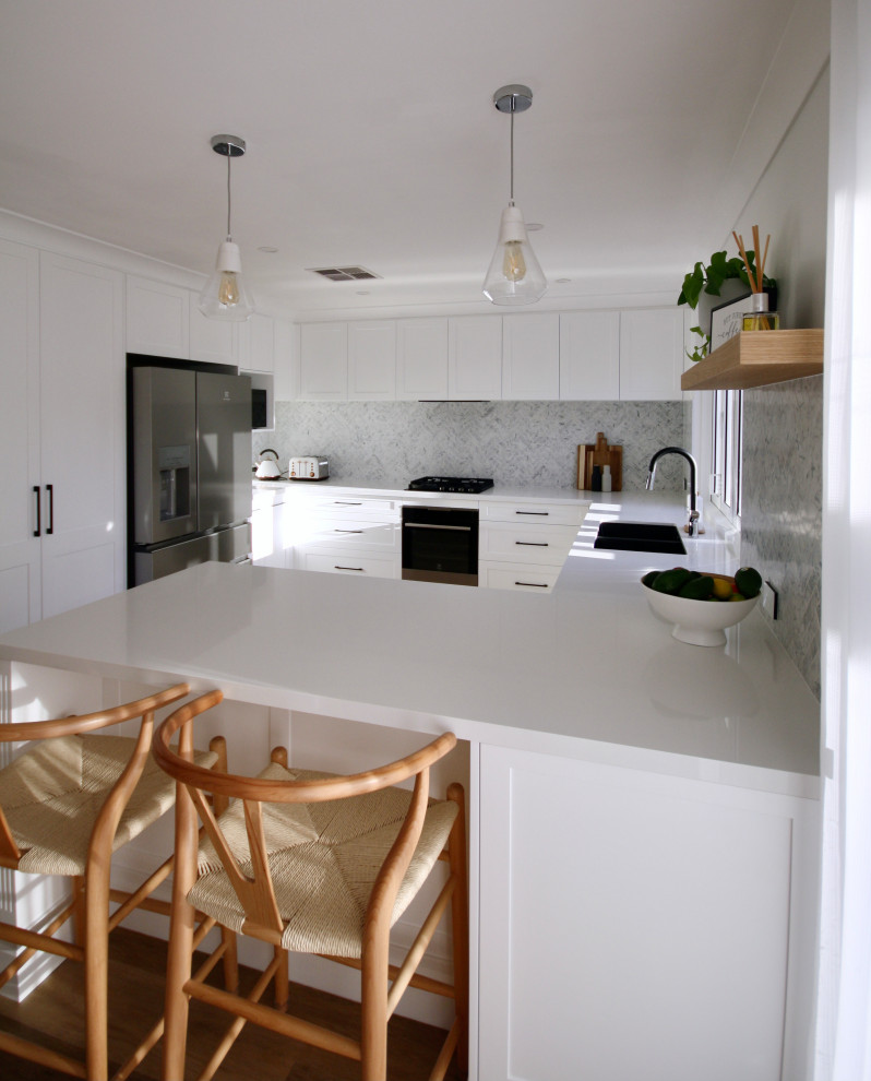 Bild på ett mellanstort funkis vit vitt kök, med en undermonterad diskho, skåp i shakerstil, vita skåp, bänkskiva i kvarts, grått stänkskydd, stänkskydd i marmor, svarta vitvaror, mellanmörkt trägolv, en köksö och brunt golv