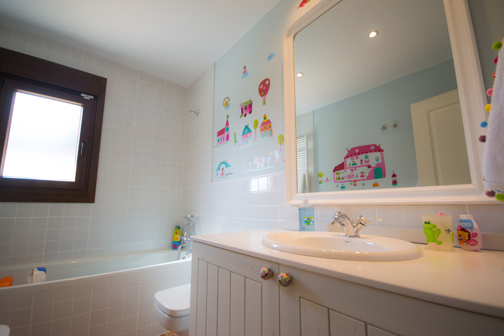 This is an example of a mid-sized traditional kids bathroom in Other with beaded inset cabinets, light wood cabinets, limestone benchtops, an alcove tub, blue tile and ceramic tile.