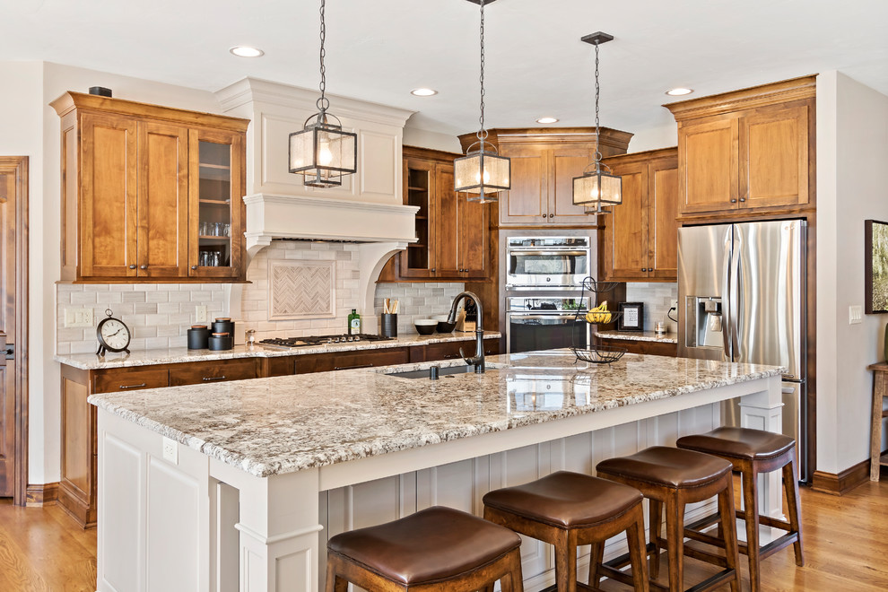Photo of a large country l-shaped open plan kitchen in Charleston with an undermount sink, shaker cabinets, medium wood cabinets, granite benchtops, beige splashback, stainless steel appliances, medium hardwood floors, with island, brown floor and multi-coloured benchtop.
