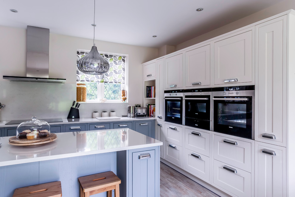 Photo of a large country u-shaped eat-in kitchen in Essex with an undermount sink, shaker cabinets, grey cabinets, quartzite benchtops, white splashback, stone slab splashback, black appliances, light hardwood floors and with island.