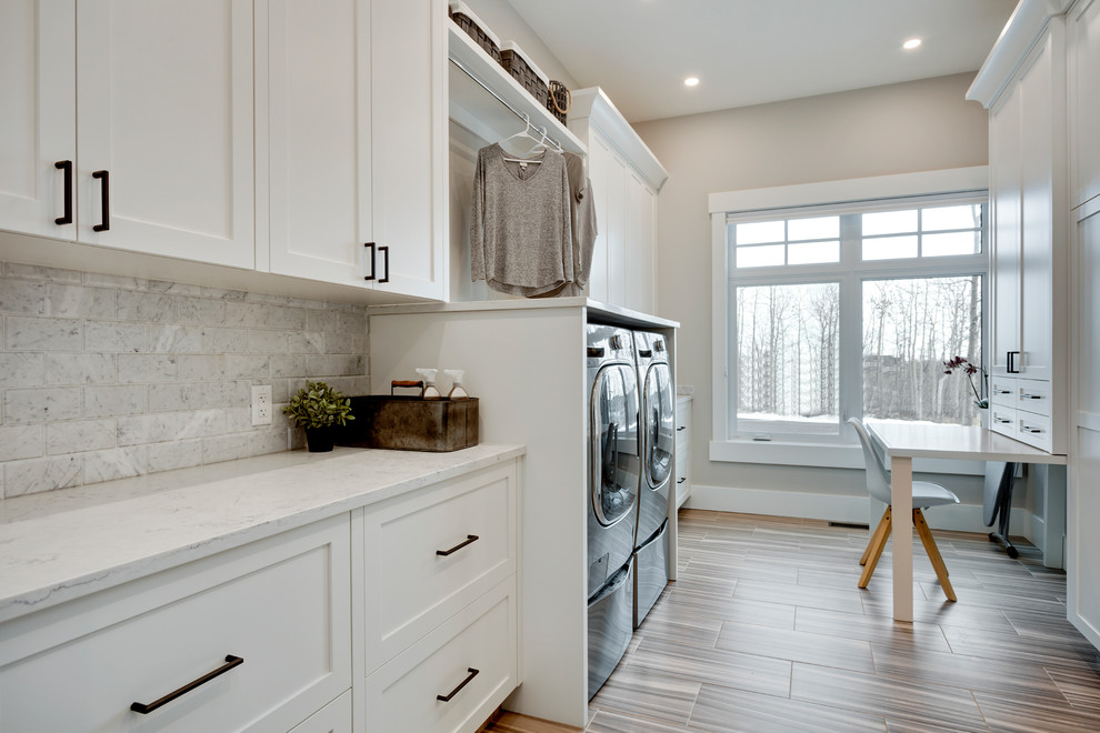 Large transitional galley dedicated laundry room in Calgary with shaker cabinets, white cabinets, quartzite benchtops, grey walls, porcelain floors, a side-by-side washer and dryer, grey floor and white benchtop.