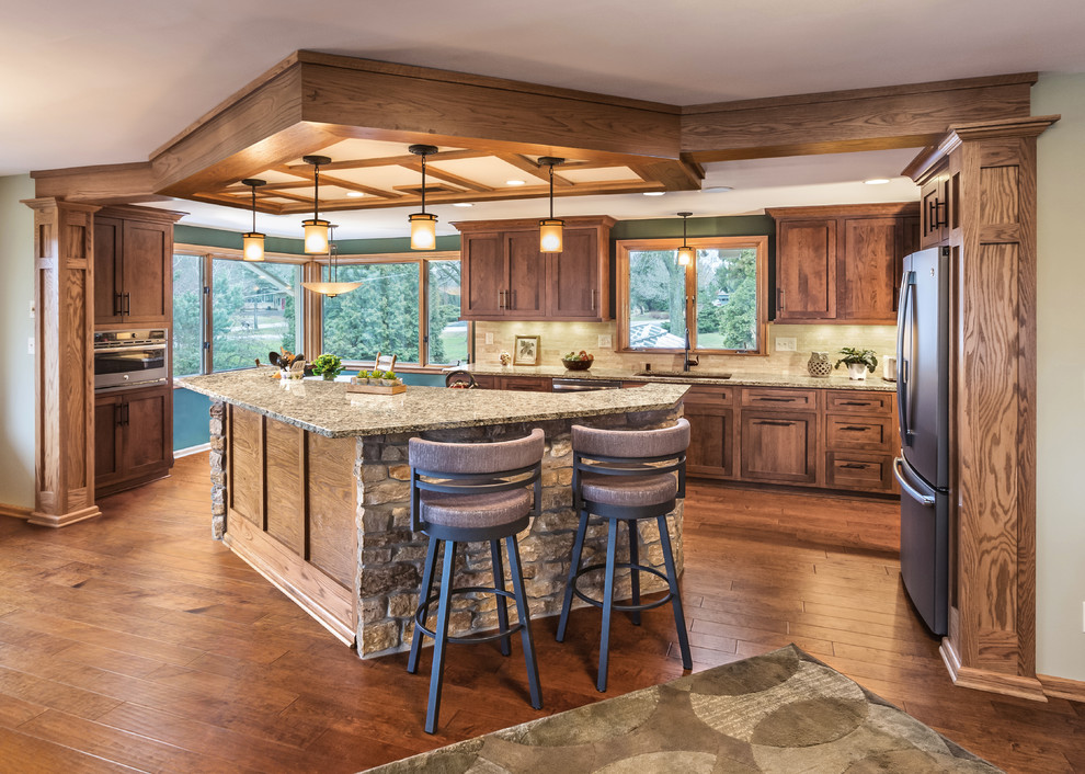 Kitchen - large traditional brown floor and medium tone wood floor kitchen idea in Milwaukee with an undermount sink, medium tone wood cabinets, granite countertops, beige backsplash, stone tile backsplash, stainless steel appliances, an island and shaker cabinets