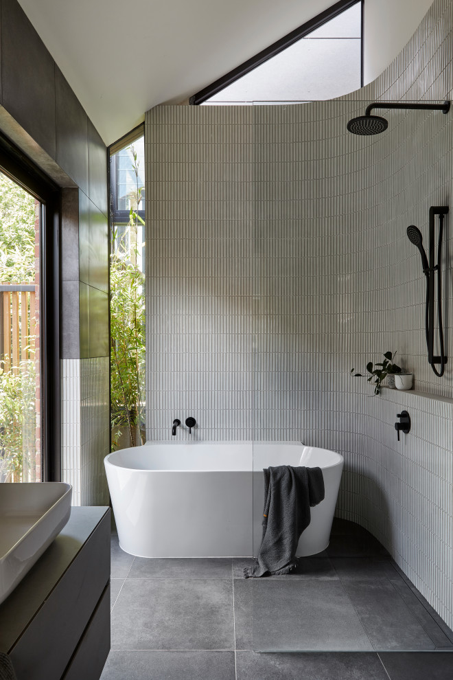Photo of a mid-sized contemporary master bathroom in Melbourne with flat-panel cabinets, grey cabinets, a freestanding tub, an open shower, a wall-mount toilet, multi-coloured tile, porcelain tile, multi-coloured walls, porcelain floors, a vessel sink, tile benchtops, grey floor, an open shower, grey benchtops, a single vanity, a built-in vanity and vaulted.