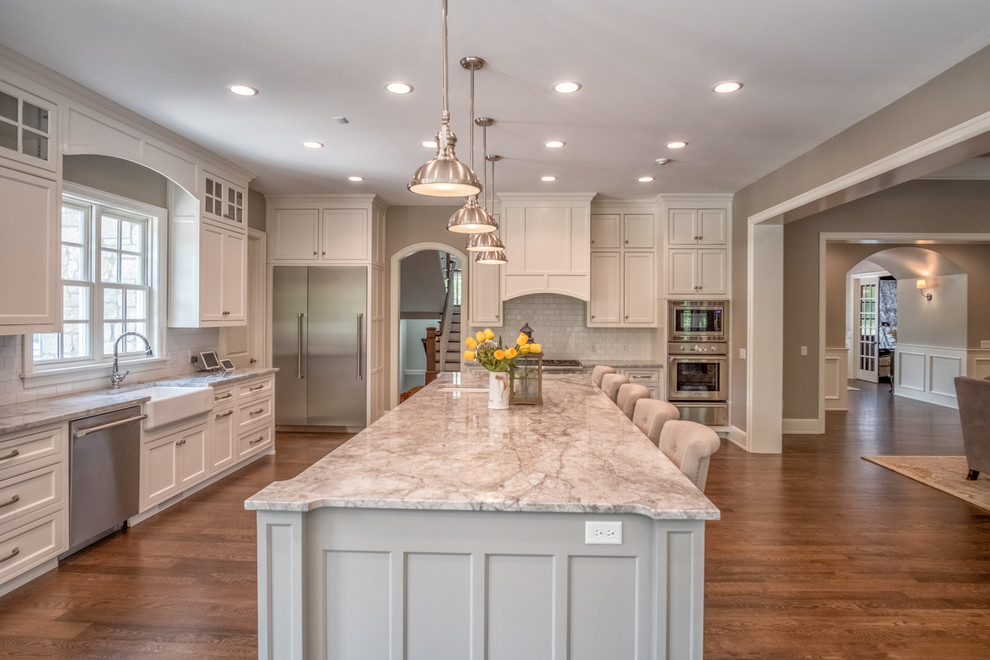 Eat-in kitchen - large transitional l-shaped medium tone wood floor eat-in kitchen idea with a farmhouse sink, shaker cabinets, white cabinets, marble countertops, white backsplash, subway tile backsplash, stainless steel appliances and an island