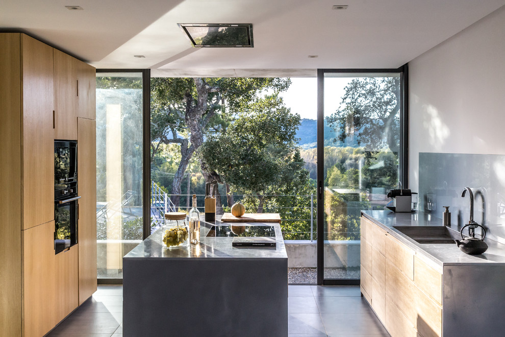 This is an example of a mid-sized contemporary galley eat-in kitchen in Nice with an integrated sink, flat-panel cabinets, medium wood cabinets, grey splashback, glass sheet splashback, black appliances, concrete floors and with island.
