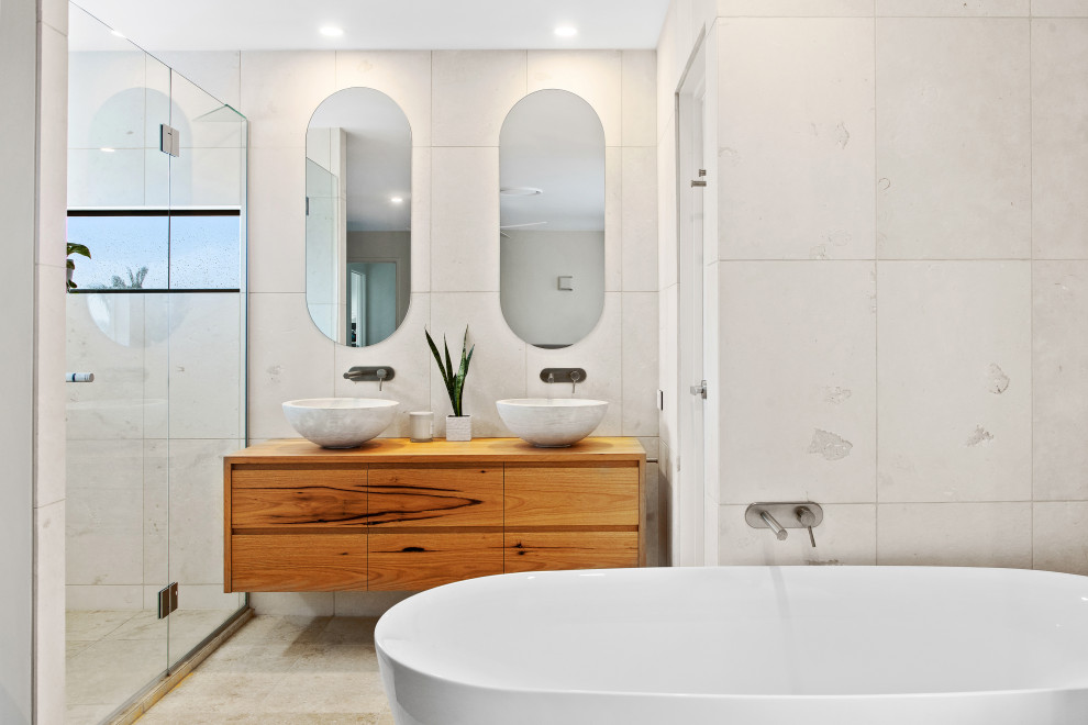 Aménagement d'une salle de bain principale bord de mer en bois clair de taille moyenne avec du carrelage en pierre calcaire, un sol en calcaire, des toilettes cachées, meuble double vasque et meuble-lavabo suspendu.