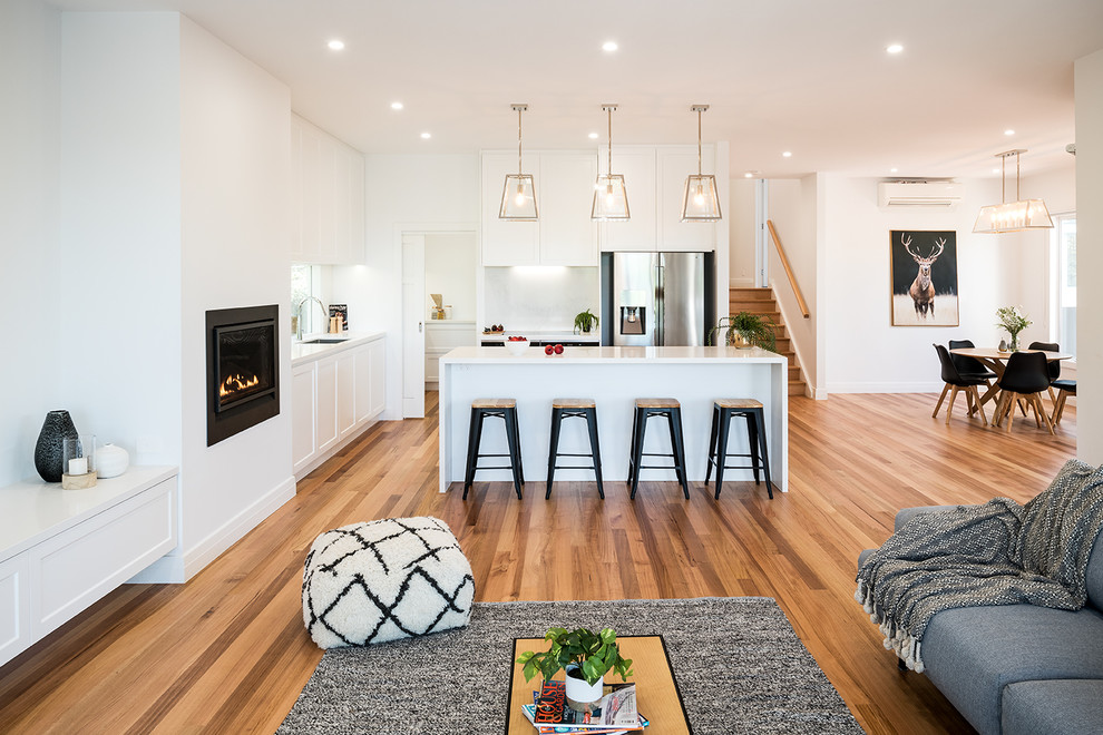 Photo of a large contemporary l-shaped open plan kitchen in Melbourne with an undermount sink, shaker cabinets, white cabinets, quartz benchtops, white splashback, glass sheet splashback, stainless steel appliances, medium hardwood floors, with island and brown floor.