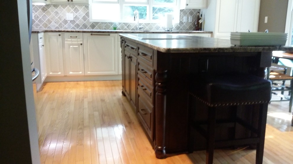 Inspiration for a mid-sized transitional l-shaped medium tone wood floor and brown floor kitchen remodel with an undermount sink, raised-panel cabinets, white cabinets, brown backsplash, ceramic backsplash, stainless steel appliances and an island