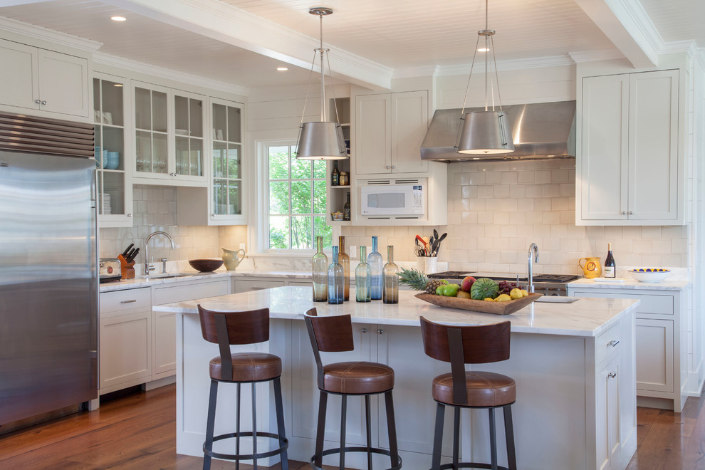 This is an example of a mid-sized beach style l-shaped kitchen in Boston with white cabinets, white splashback, stainless steel appliances, with island, shaker cabinets and medium hardwood floors.