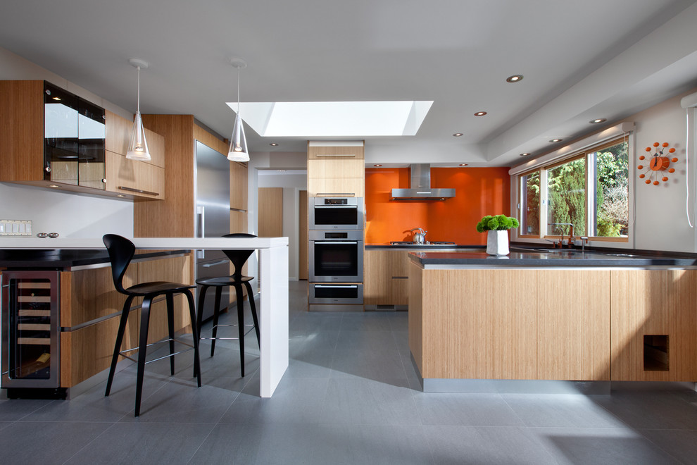 This is an example of a mid-sized midcentury u-shaped eat-in kitchen in Vancouver with orange splashback, glass sheet splashback, flat-panel cabinets, light wood cabinets, concrete benchtops, stainless steel appliances, an undermount sink, ceramic floors, a peninsula and grey floor.