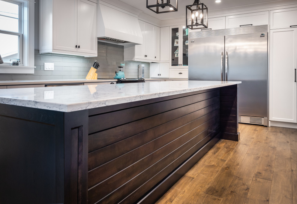 Kitchen - large transitional l-shaped medium tone wood floor and brown floor kitchen idea with an undermount sink, white cabinets, quartz countertops, white backsplash, glass tile backsplash, stainless steel appliances, an island and white countertops