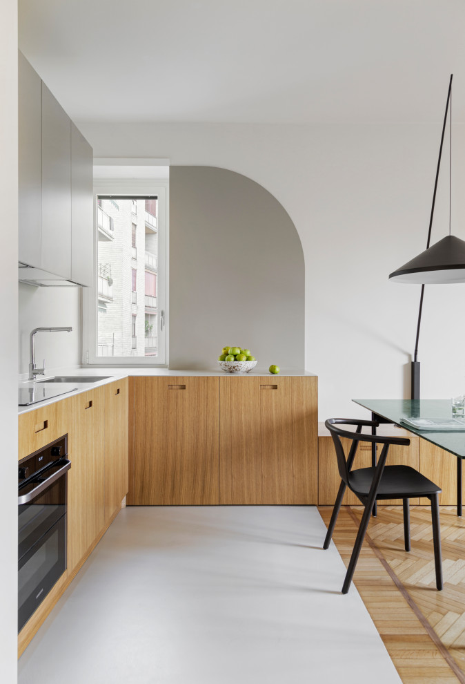 Inspiration for a mid-sized contemporary l-shaped open plan kitchen in Milan with an undermount sink, flat-panel cabinets, light wood cabinets, solid surface benchtops, grey splashback, concrete floors, grey floor and white benchtop.