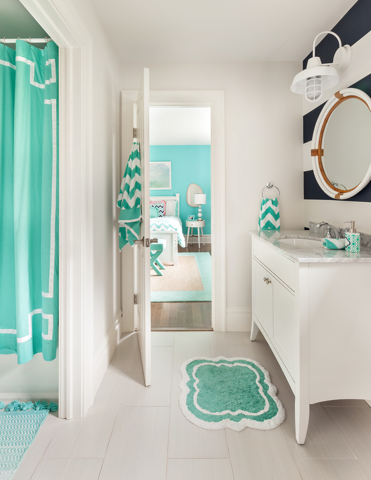 This is an example of a mid-sized transitional kids bathroom in New York with shaker cabinets, white cabinets, a shower/bathtub combo, a two-piece toilet, white tile, ceramic tile, porcelain floors, an undermount sink, marble benchtops, multi-coloured walls and a shower curtain.