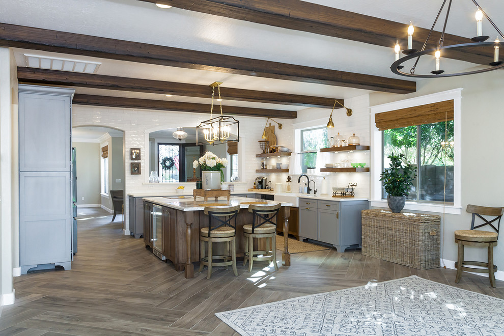 Large transitional l-shaped porcelain tile and brown floor eat-in kitchen photo in Phoenix with a farmhouse sink, shaker cabinets, gray cabinets, quartz countertops, white backsplash, glass sheet backsplash, stainless steel appliances, an island and white countertops