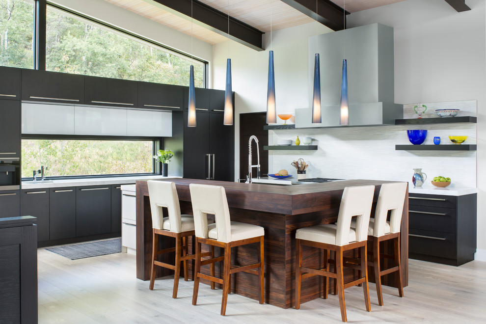 Photo of a contemporary l-shaped kitchen in Denver with flat-panel cabinets, black cabinets, wood benchtops, grey splashback, panelled appliances, light hardwood floors, with island and grey floor.