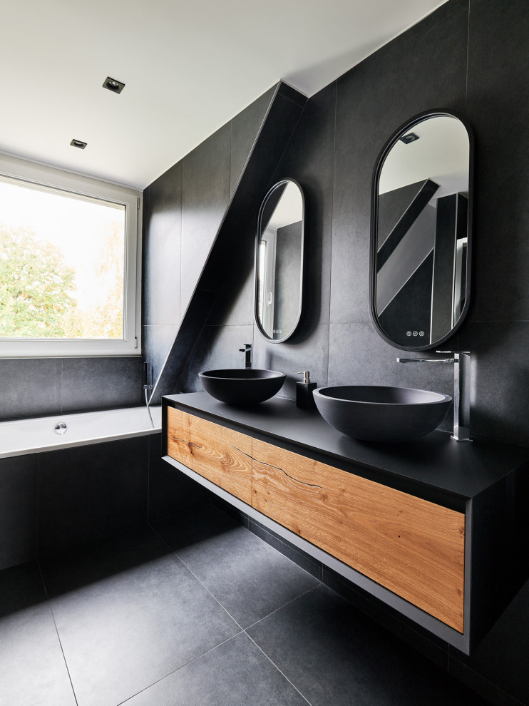 Large contemporary bathroom in Paris with medium wood cabinets, an undermount tub, a wall-mount toilet, black tile, ceramic tile, black walls, ceramic floors, a drop-in sink, solid surface benchtops, black floor, a sliding shower screen, a double vanity, a floating vanity and flat-panel cabinets.