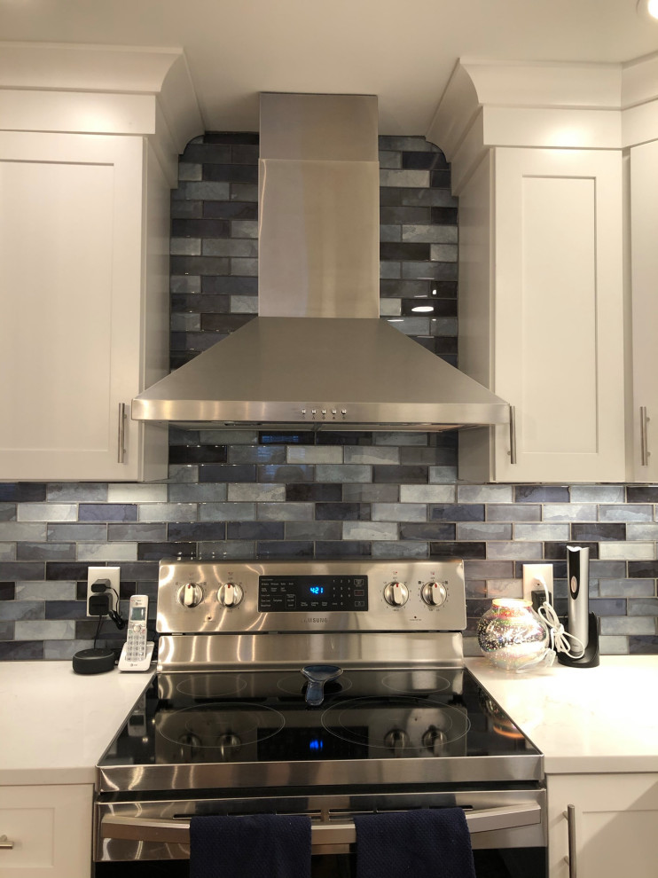Photo of a mid-sized traditional galley open plan kitchen in Bridgeport with an undermount sink, shaker cabinets, white cabinets, quartz benchtops, blue splashback, glass tile splashback, stainless steel appliances, light hardwood floors, with island, multi-coloured floor and white benchtop.