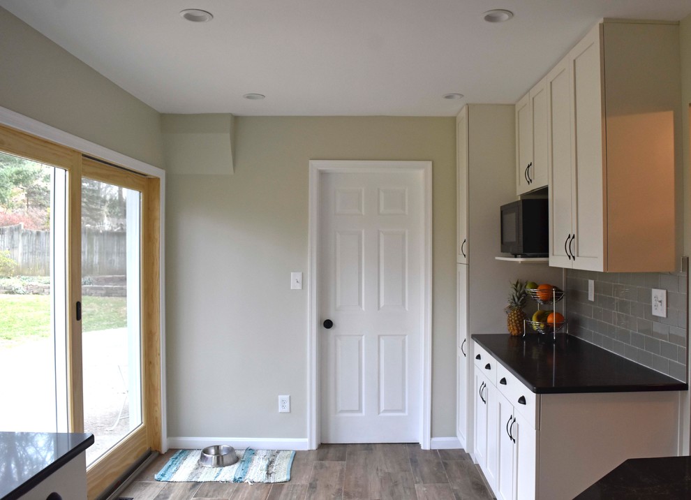 Inspiration for a mid-sized transitional galley laminate floor and brown floor enclosed kitchen remodel in DC Metro with a farmhouse sink, shaker cabinets, white cabinets, granite countertops, gray backsplash, subway tile backsplash, stainless steel appliances, no island and black countertops