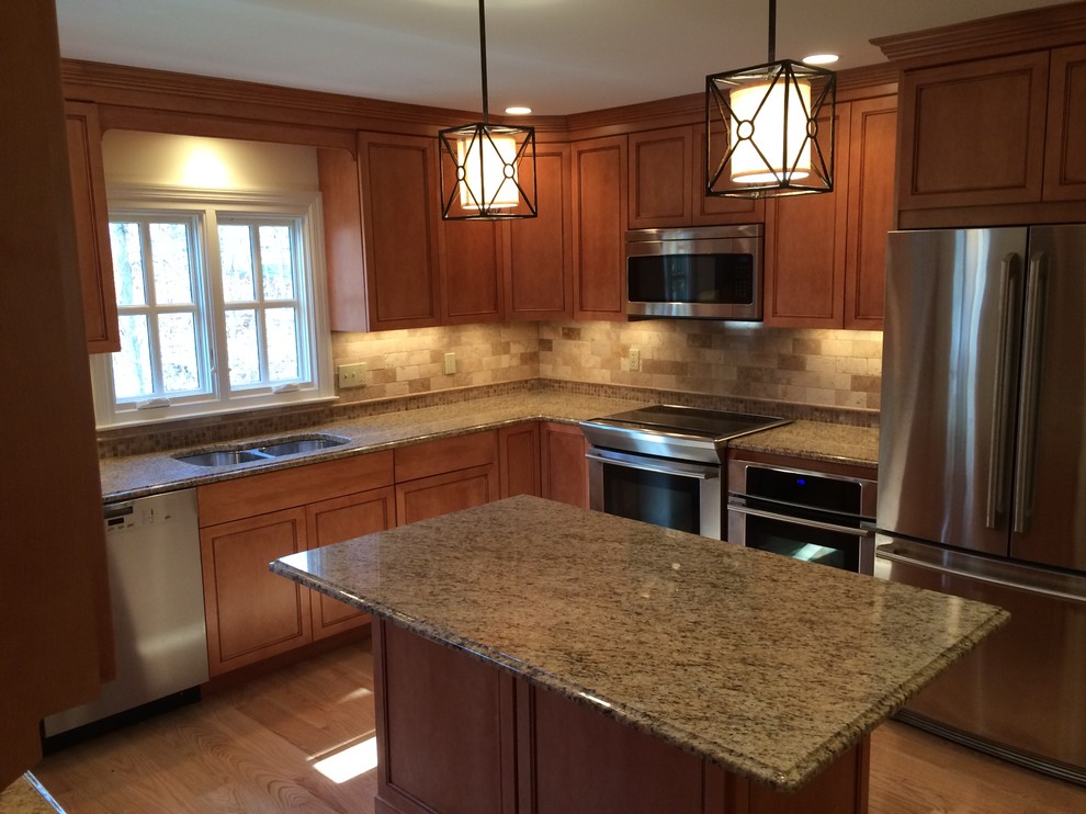 Photo of a transitional u-shaped kitchen in New York with an undermount sink, shaker cabinets, medium wood cabinets, granite benchtops, beige splashback, stone tile splashback, stainless steel appliances, light hardwood floors and with island.