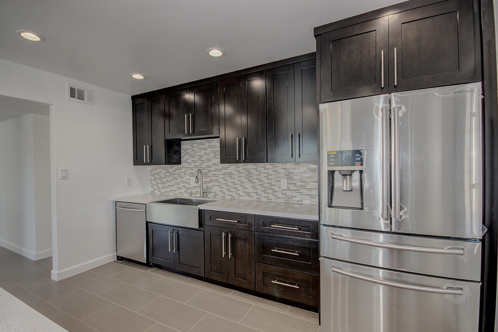Mid-sized transitional single-wall porcelain tile eat-in kitchen photo in Phoenix with a farmhouse sink, shaker cabinets, dark wood cabinets, quartz countertops, multicolored backsplash, glass sheet backsplash, stainless steel appliances and an island
