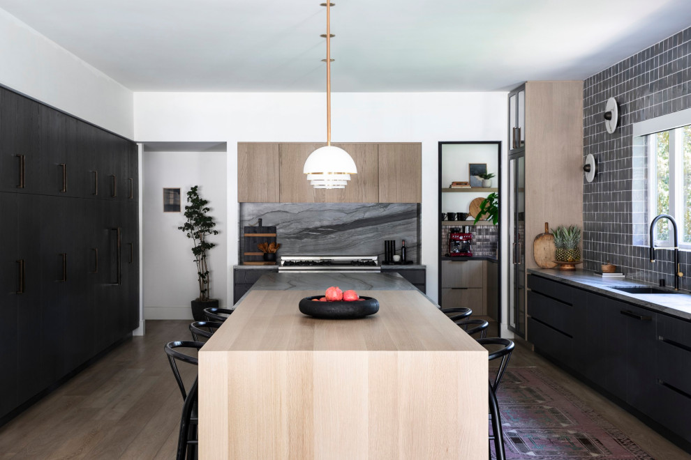 Contemporary u-shaped kitchen in Orange County with a submerged sink, flat-panel cabinets, black cabinets, grey splashback, light hardwood flooring, an island, beige floors and grey worktops.