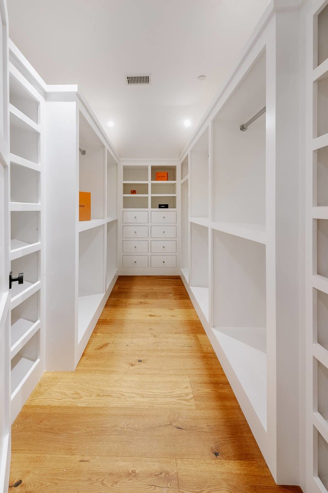 Design ideas for a mid-sized country gender-neutral walk-in wardrobe in Los Angeles with open cabinets, white cabinets, medium hardwood floors and brown floor.