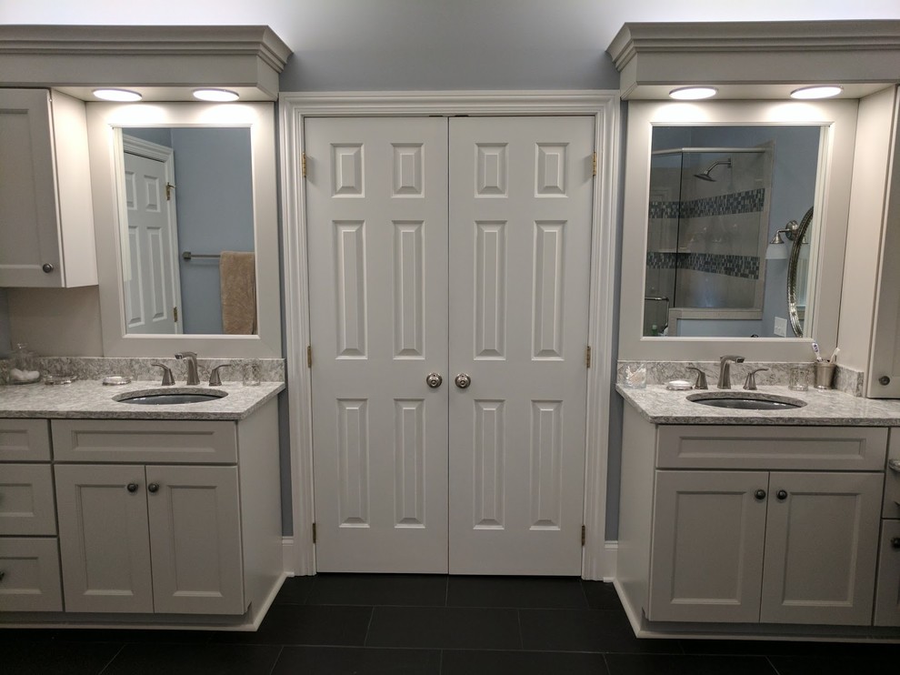 Design ideas for a traditional bathroom in Charlotte with shaker cabinets, grey cabinets, a freestanding tub, a corner shower, gray tile, stone tile, porcelain floors, an undermount sink, black floor and a hinged shower door.