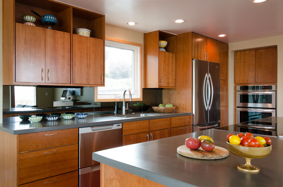 Mid-sized midcentury l-shaped eat-in kitchen in Seattle with a single-bowl sink, flat-panel cabinets, medium wood cabinets, solid surface benchtops, with island, mirror splashback and stainless steel appliances.