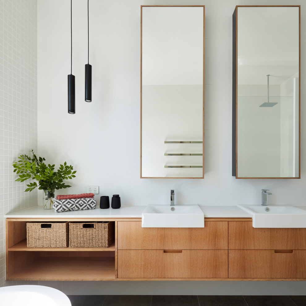 This is an example of a mid-sized contemporary master bathroom in Adelaide with light wood cabinets, a freestanding tub, a one-piece toilet, white tile, ceramic tile, white walls, ceramic floors, a drop-in sink, grey floor, an open shower, white benchtops, a double vanity, an open shower, engineered quartz benchtops, a floating vanity and flat-panel cabinets.