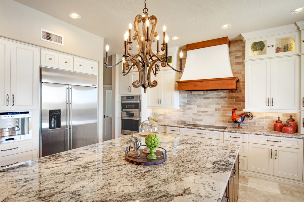 Example of a large transitional u-shaped travertine floor and beige floor open concept kitchen design in Phoenix with recessed-panel cabinets, white cabinets, granite countertops, an island, multicolored countertops, a farmhouse sink, gray backsplash, porcelain backsplash and stainless steel appliances