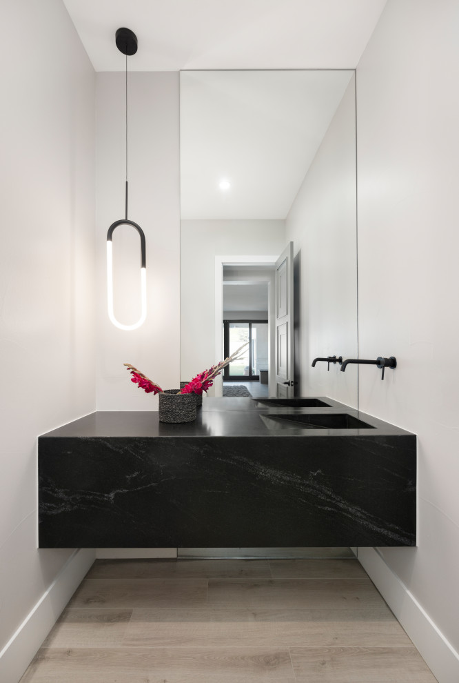 This is an example of a medium sized contemporary cloakroom in Denver with a one-piece toilet, mirror tiles, grey walls, laminate floors, an integrated sink, granite worktops, grey floors, black worktops and a floating vanity unit.