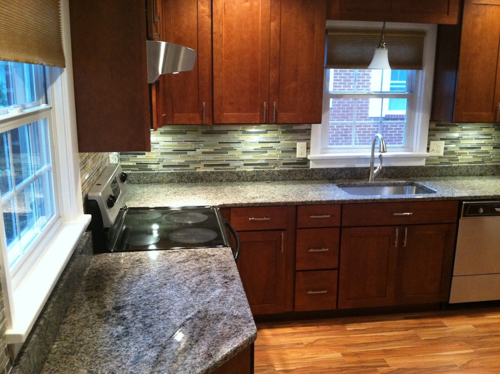 Example of a transitional l-shaped vinyl floor kitchen design with an undermount sink, shaker cabinets, medium tone wood cabinets, granite countertops, multicolored backsplash, mosaic tile backsplash and stainless steel appliances