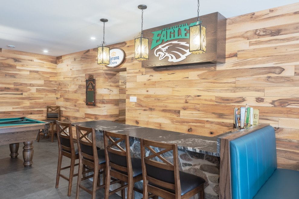 Example of a large mountain style walk-out vinyl floor, gray floor, exposed beam and wood wall basement design with a bar, multicolored walls, a standard fireplace and a stone fireplace