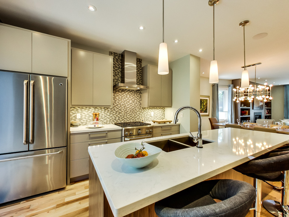 Inspiration for a mid-sized transitional galley light wood floor and multicolored floor kitchen remodel in Toronto with a double-bowl sink, flat-panel cabinets, beige cabinets, quartz countertops, gray backsplash, ceramic backsplash, stainless steel appliances and an island