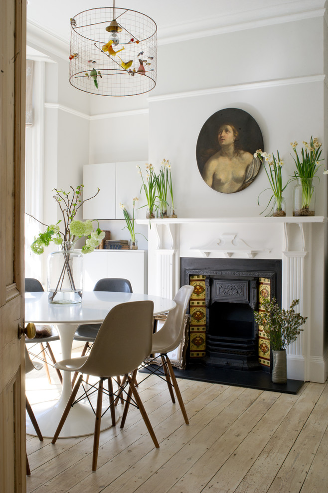 Eclectic dining room in London with grey walls, light hardwood floors and a standard fireplace.