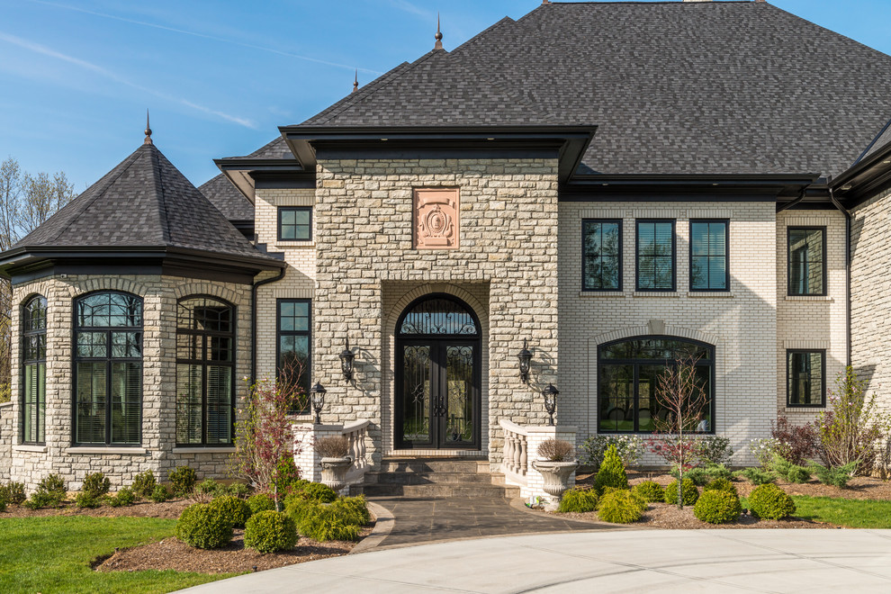 This is an example of a mid-sized traditional two-storey beige house exterior in Cincinnati with stone veneer, a gable roof and a tile roof.