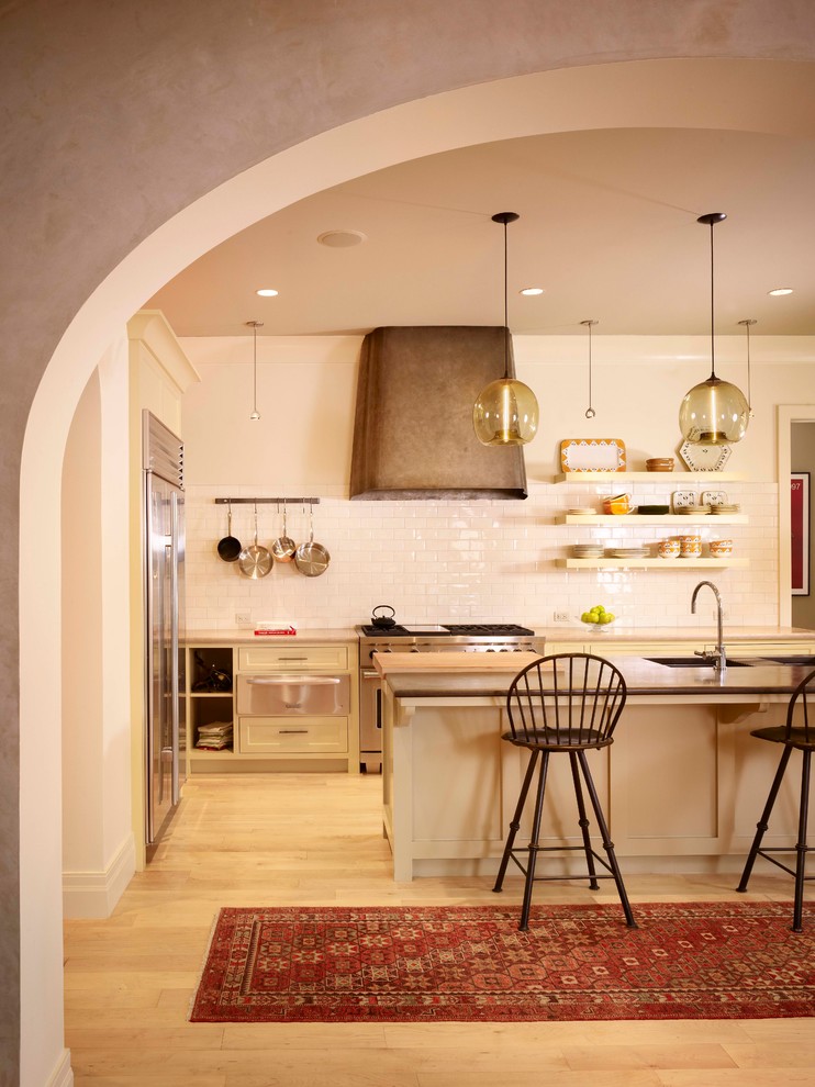 Inspiration for a mediterranean kitchen in Austin with shaker cabinets, beige cabinets, white splashback, subway tile splashback, stainless steel appliances, light hardwood floors and with island.
