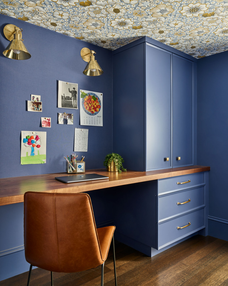 This is an example of a large transitional study room in Manchester with blue walls, medium hardwood floors, no fireplace, a built-in desk, brown floor, wallpaper and panelled walls.