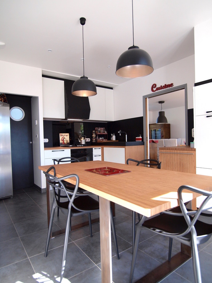 Photo of a mid-sized modern l-shaped separate kitchen in Brest with a double-bowl sink, beaded inset cabinets, white cabinets, wood benchtops, black splashback, slate splashback, black appliances, ceramic floors, no island and grey floor.