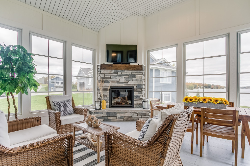 Photo of a beach style sunroom in Other with a corner fireplace, a stone fireplace surround, a standard ceiling and grey floor.