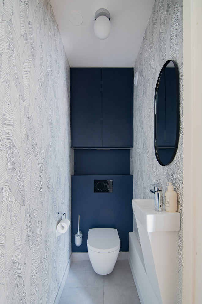 Inspiration for a mid-sized modern powder room in Paris with a wall-mount toilet, grey walls, cement tiles, a wall-mount sink, wood benchtops, blue benchtops, a floating vanity and wallpaper.