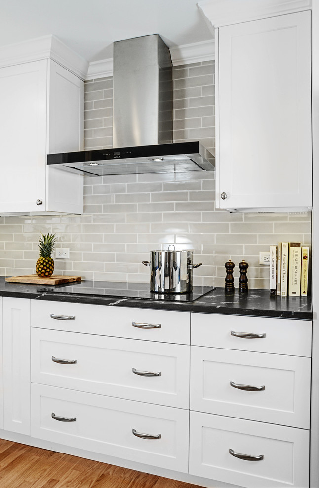 Mid-sized transitional u-shaped medium tone wood floor eat-in kitchen photo with a farmhouse sink, shaker cabinets, white cabinets, onyx countertops, gray backsplash, subway tile backsplash, stainless steel appliances and an island