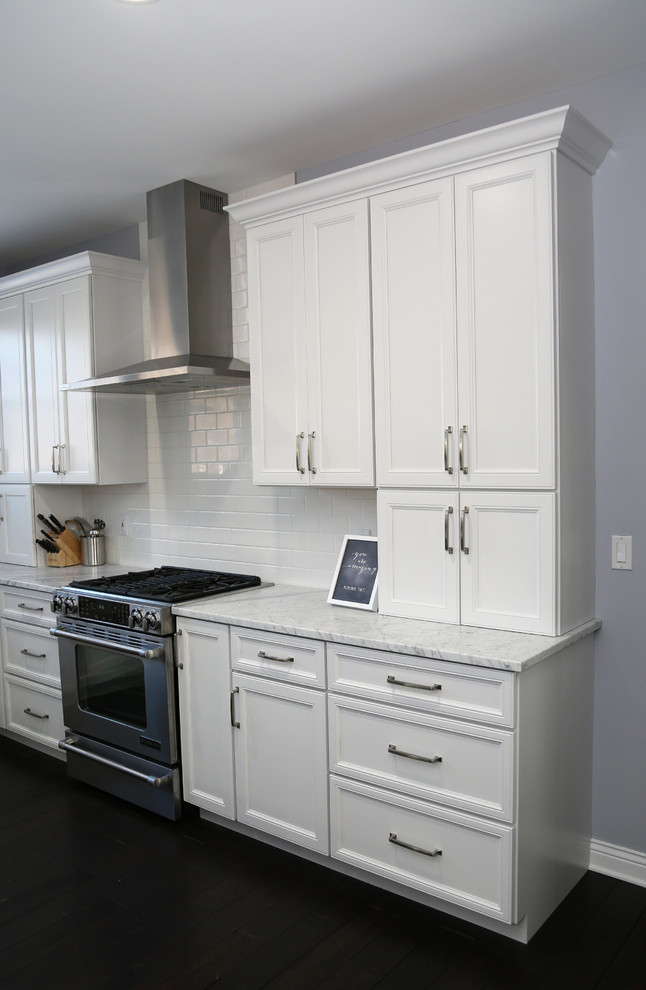 Example of a large transitional l-shaped dark wood floor eat-in kitchen design in Chicago with recessed-panel cabinets, stainless steel appliances, an island, a farmhouse sink, white cabinets, quartz countertops, white backsplash and subway tile backsplash