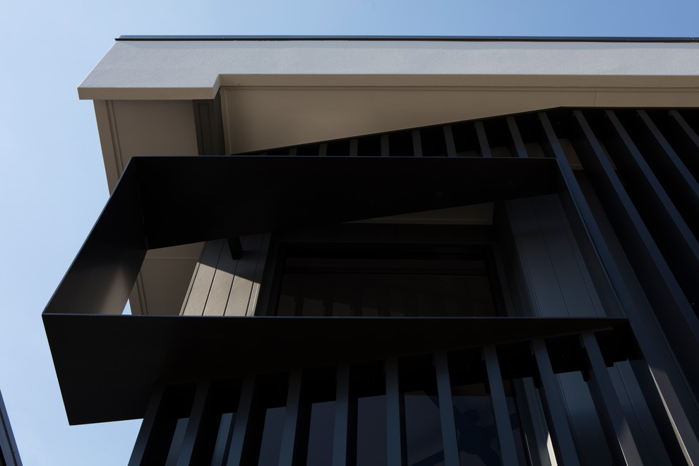 This is an example of a contemporary two-storey black house exterior in Brisbane with metal siding, a flat roof and a metal roof.