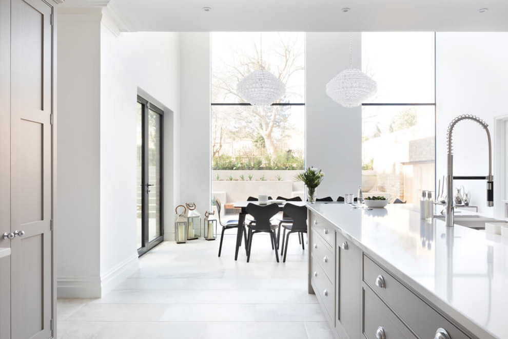 This is an example of a large modern u-shaped open plan kitchen in London with shaker cabinets, grey cabinets, quartzite benchtops, white splashback, marble splashback, stainless steel appliances, marble floors, with island, beige floor and white benchtop.